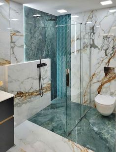 a bathroom with marble walls and flooring is pictured in this image, it has a glass shower stall