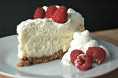 a white plate topped with a slice of cheesecake and raspberries on top of it