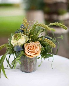 an arrangement of flowers in a metal vase on a white tablecloth with greenery