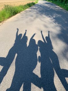 the shadow of three people on the road with their arms in the air and one person standing behind them