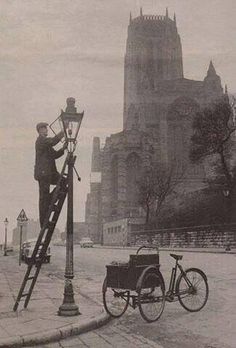 an old photo of a man working on a lamp post