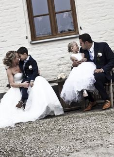 a bride and groom are sitting on a bench with their two children in front of a white building