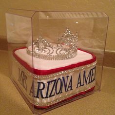 a cake in a glass case with a tiara on top and red velvet under it