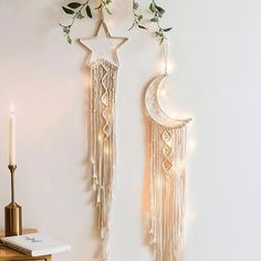 two wall hangings decorated with lights and greenery next to a candle holder on a table