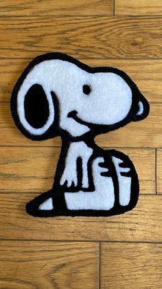 a black and white patch with a snoopy dog on it's side sitting on a wooden floor