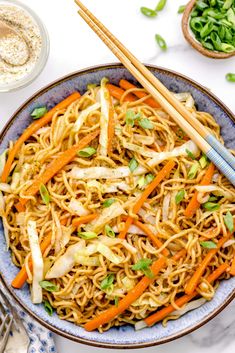 a bowl filled with noodles, carrots and green onions next to chopsticks