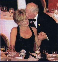 an older man and woman sitting at a table with wine glasses in front of them