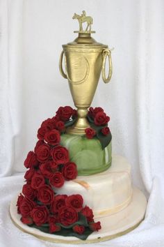 a three tiered cake decorated with red roses and a gold trophy on the top