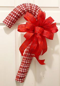 a red and white wreath on the front door with ribbon hanging from it's side