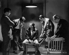 four men in suits and ties standing around a chair