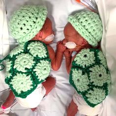 two newborn babies wearing green crocheted hats and diapers with pacifiers in their mouths