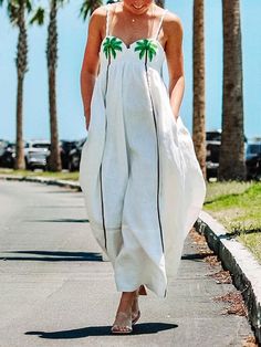 a woman walking down the street in a white dress with green palm trees on it