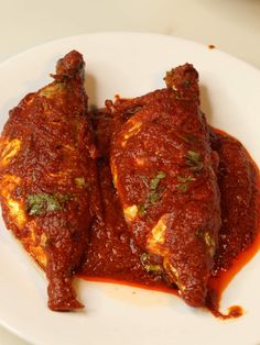 two pieces of meat covered in sauce on a white plate