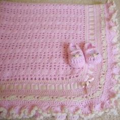 a pink crocheted blanket and pair of baby shoes sitting on the floor next to it