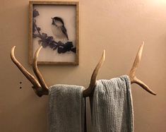 deer antlers hang on the wall next to two towels and a framed picture in a bathroom