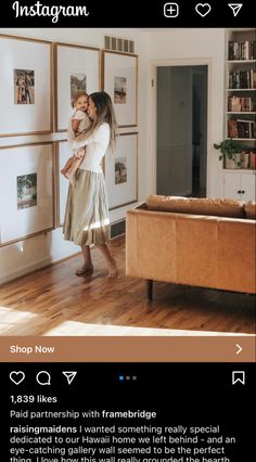 a woman holding a baby in her arms while standing next to a wall with pictures on it