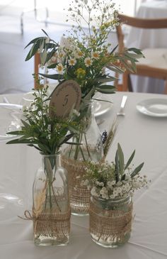 three vases with flowers are sitting on a table in front of a white table cloth