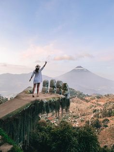 a woman standing on top of a cliff with her arms in the air