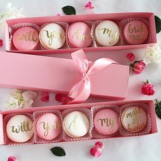 two pink boxes filled with macaroons on top of a bed of flowers next to each other