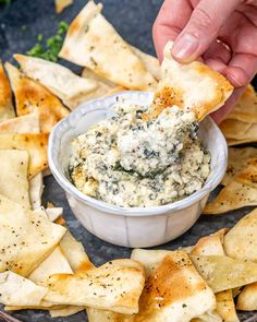 a hand dipping a tortilla chip into a bowl of spinach artichoke dip