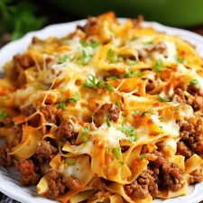 a white plate topped with pasta covered in ground beef and cheese on top of a wooden table