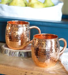 two copper mugs sitting on top of a wooden table