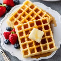 two waffles with butter and blueberries on a white plate next to strawberries