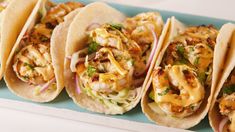 several tacos are lined up on a blue platter with shrimp and cole slaw