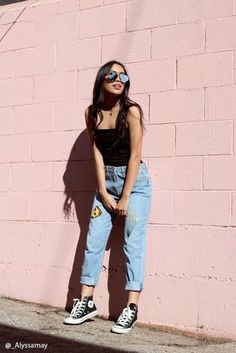 a woman standing in front of a pink wall with her hands on her hips wearing sunglasses