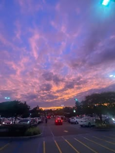 a parking lot filled with lots of parked cars under a purple and blue cloudy sky