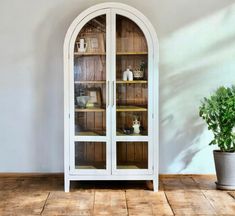 a white china cabinet sitting on top of a wooden floor next to a potted plant