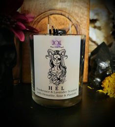 a candle with a label on it sitting next to some flowers and a wooden plaque