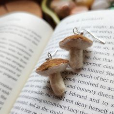 two tiny mushrooms sitting on top of an open book with silver earwires attached to them