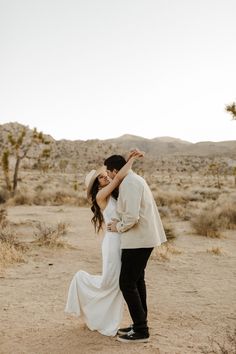 a man and woman are standing in the desert with their arms around each other as they dance