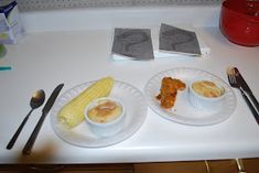 two plates with corn on the cob and other food sitting on a counter top