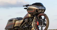 a black and red motorcycle parked on the side of a road with clouds in the background