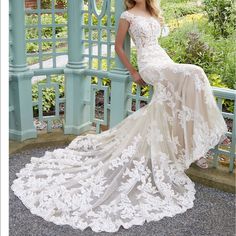 a woman in a wedding dress leaning against a fence with her hand on her hip