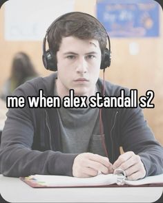 a young man wearing headphones sitting at a desk with a book and notebook in front of him