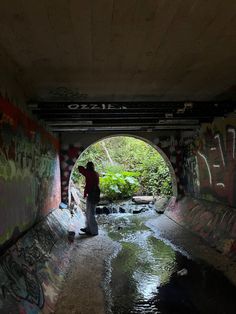 a man standing in the middle of a tunnel with graffiti on it and water running underneath