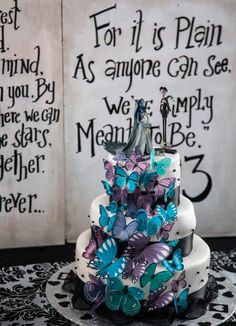 a wedding cake decorated with butterflies on a black and white tablecloth next to two book pages