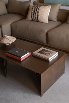 a coffee table with two books on it in front of a couch and pillows behind it