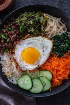 an egg is on top of rice, carrots, cucumbers and other vegetables