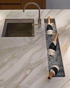 two bottles of wine sitting on top of a marble countertop next to a sink