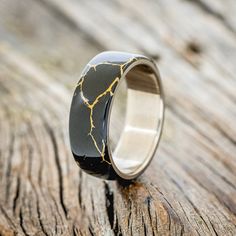 a black and gold wedding ring on top of a wooden table with cracks in it