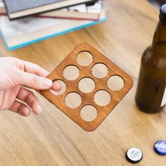 a person is holding a wooden coaster with holes in it and some beer bottle caps on the table