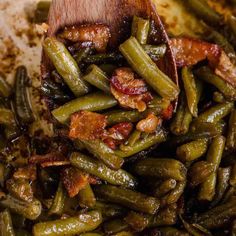 cooked green beans with bacon in a skillet being stirred by a wooden spatula