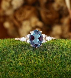 a ring with an oval blue topaz surrounded by diamonds on green grass in front of a teddy bear