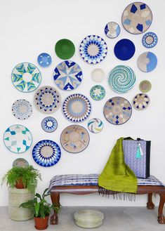 a wall with many plates on it and a bench in the foreground, next to potted plants