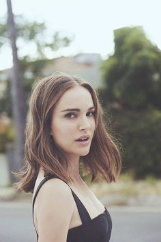 a woman with shoulder length brown hair wearing a black dress and looking at the camera