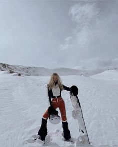 a woman standing in the snow with her snowboard